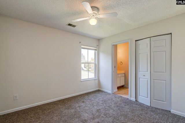 unfurnished bedroom with ceiling fan, a textured ceiling, ensuite bathroom, a closet, and light colored carpet