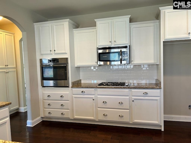 kitchen with white cabinets, backsplash, appliances with stainless steel finishes, dark hardwood / wood-style flooring, and dark stone counters