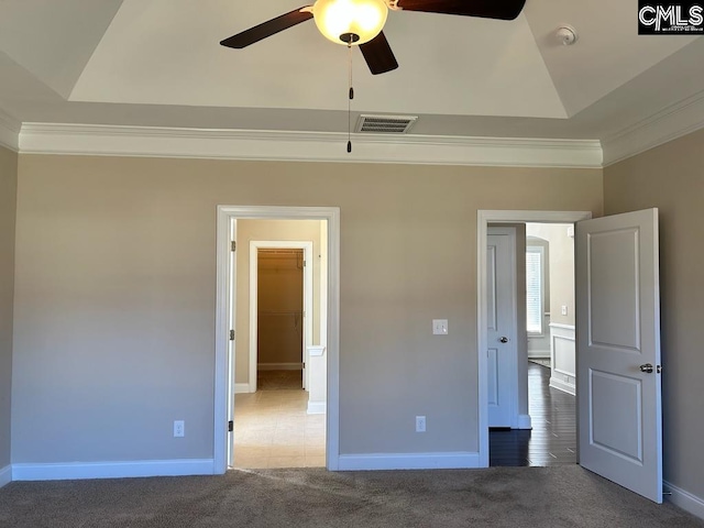 unfurnished bedroom with a spacious closet, crown molding, ceiling fan, and dark colored carpet