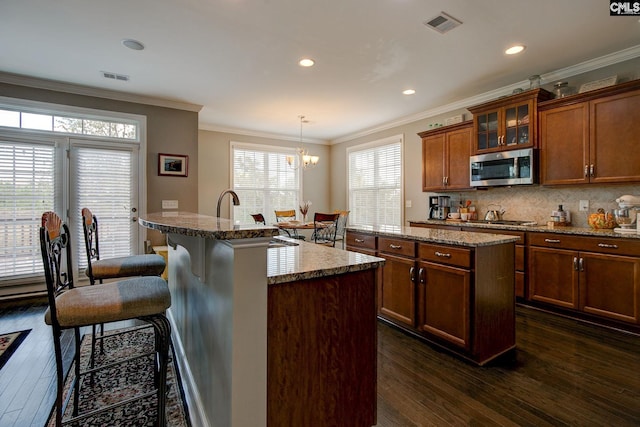 kitchen with appliances with stainless steel finishes, dark hardwood / wood-style floors, an island with sink, hanging light fixtures, and crown molding