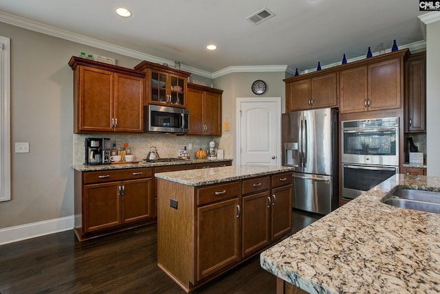 kitchen featuring appliances with stainless steel finishes, ornamental molding, light stone countertops, a kitchen island, and dark hardwood / wood-style flooring