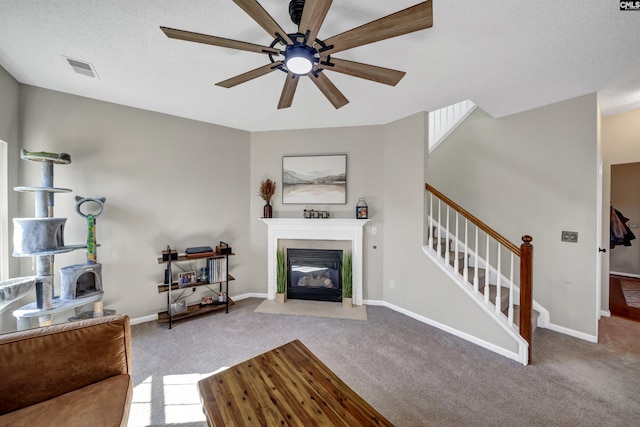 living area with stairs, a ceiling fan, a fireplace with flush hearth, and carpet