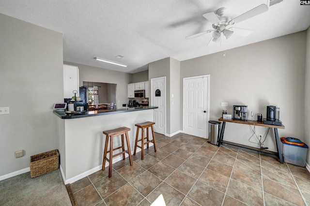 kitchen with ceiling fan, a kitchen bar, dark countertops, white cabinets, and stainless steel microwave