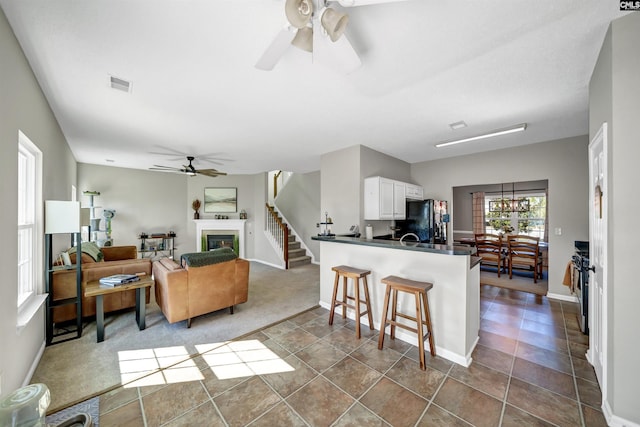 kitchen with dark countertops, freestanding refrigerator, a ceiling fan, white cabinetry, and visible vents