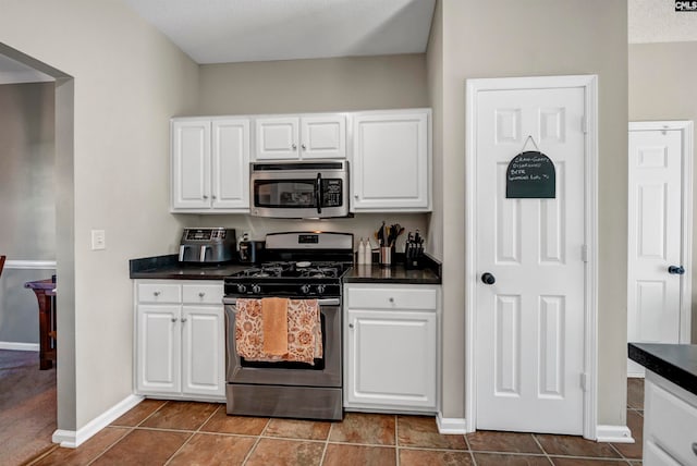 kitchen featuring dark tile patterned flooring, appliances with stainless steel finishes, a textured ceiling, and white cabinets