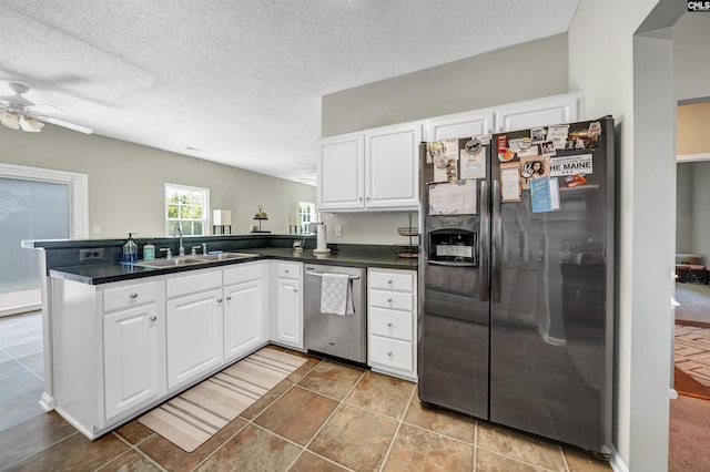 kitchen with a ceiling fan, dark countertops, a sink, a peninsula, and stainless steel appliances