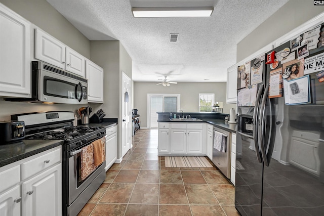 kitchen featuring stainless steel appliances, dark countertops, a sink, and a peninsula