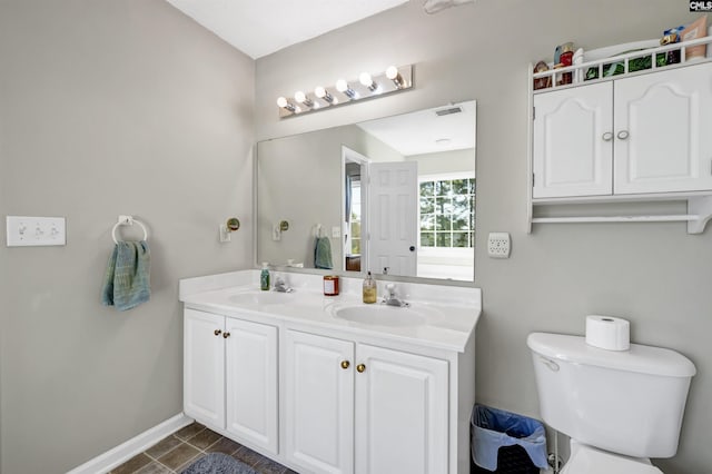 bathroom featuring toilet, double vanity, baseboards, and a sink