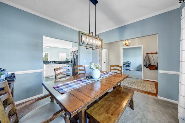 carpeted dining area featuring crown molding, baseboards, a sink, and a notable chandelier
