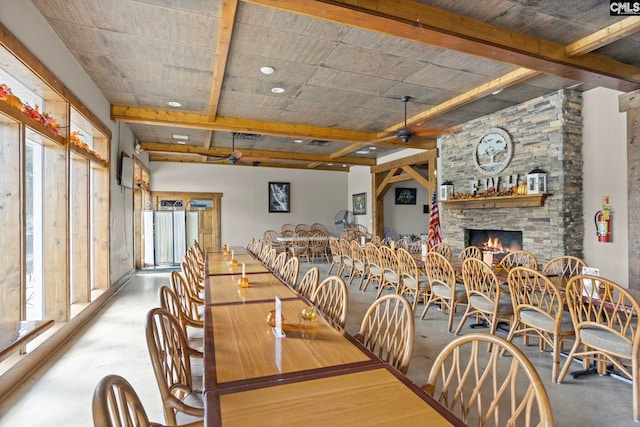 dining room featuring a stone fireplace, concrete floors, plenty of natural light, and ceiling fan