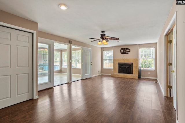 unfurnished living room featuring a tiled fireplace, dark hardwood / wood-style floors, and ceiling fan