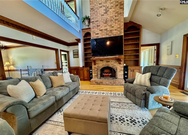 living room with built in features, a fireplace, high vaulted ceiling, and light wood-type flooring