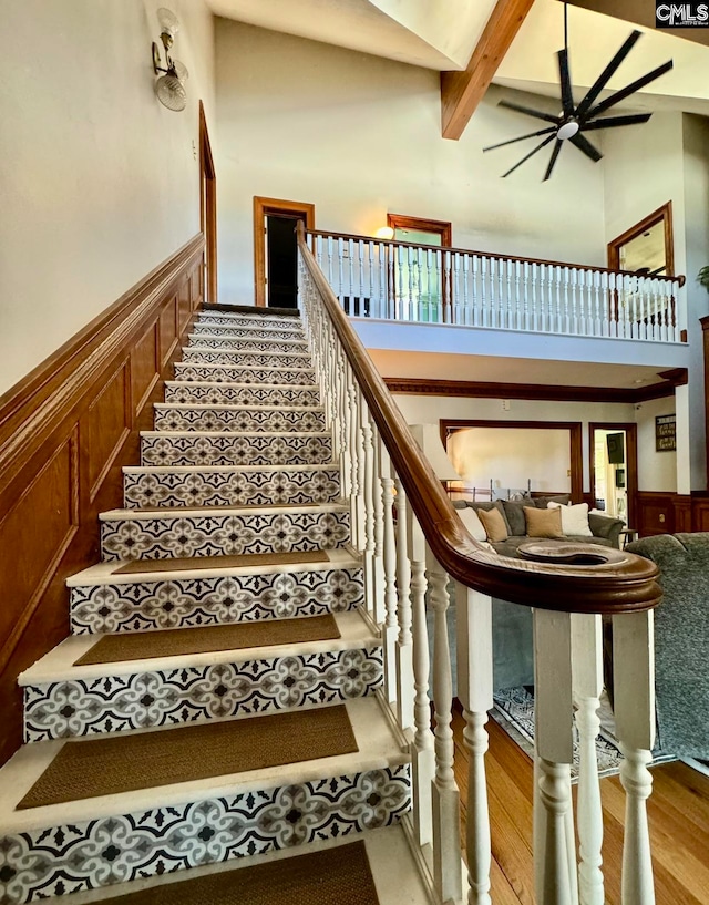 stairs with hardwood / wood-style floors, beamed ceiling, and a high ceiling