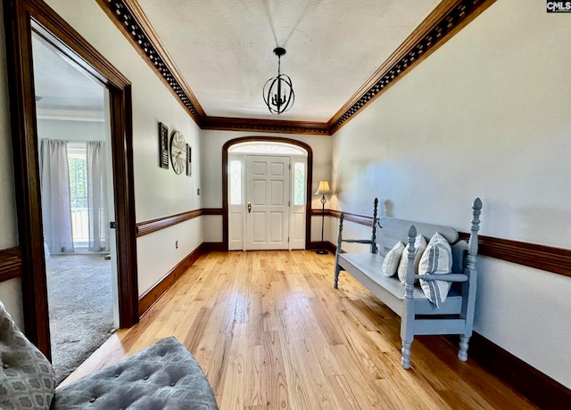 entryway featuring ornamental molding, a chandelier, a textured ceiling, and light wood-type flooring