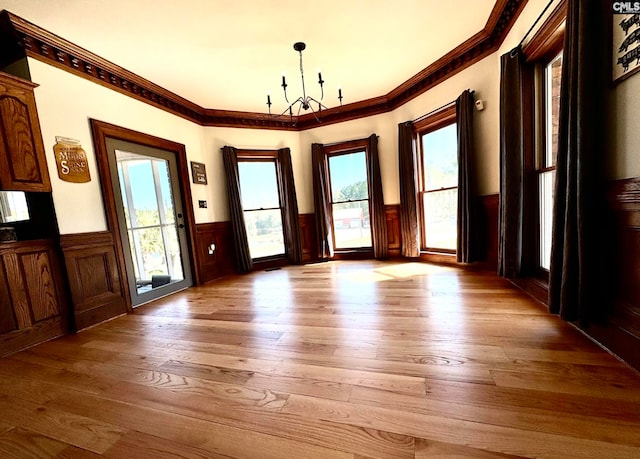 doorway with light hardwood / wood-style floors, an inviting chandelier, ornamental molding, and a healthy amount of sunlight