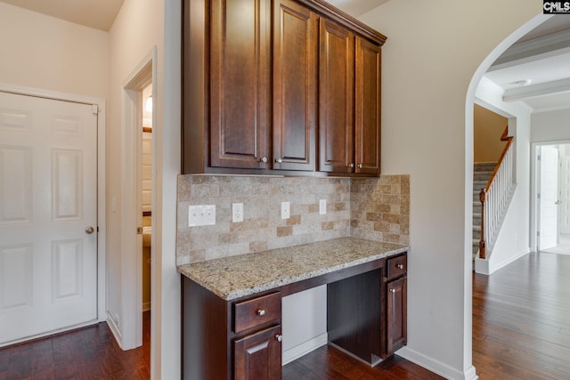 kitchen featuring decorative backsplash, built in desk, light stone counters, and dark hardwood / wood-style flooring