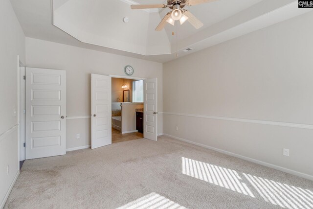 unfurnished bedroom with connected bathroom, a tray ceiling, light colored carpet, and ceiling fan