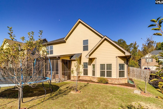 rear view of property with a yard, a trampoline, and a sunroom