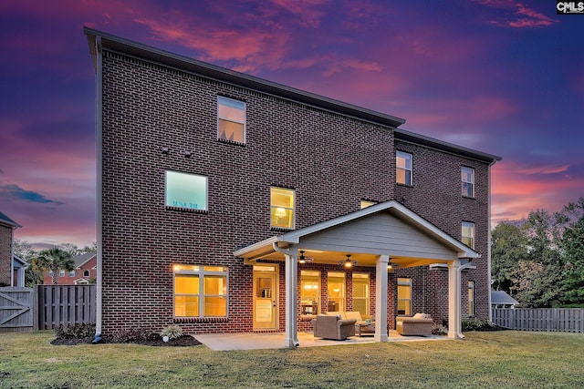 back house at dusk with a patio, an outdoor living space, a lawn, and ceiling fan