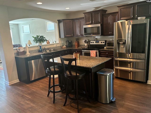 kitchen featuring a kitchen island, dark wood-type flooring, stainless steel appliances, a kitchen bar, and stone counters