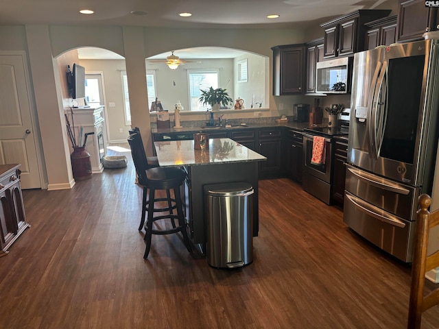 kitchen featuring a kitchen island, stone countertops, stainless steel appliances, dark wood-type flooring, and a breakfast bar area