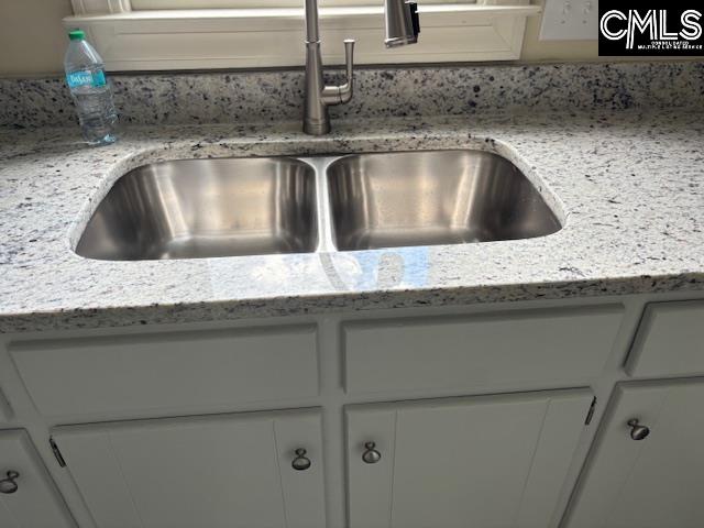 interior details with white cabinets, light stone countertops, and sink