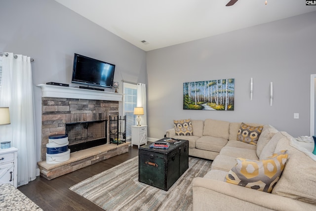 living room featuring ceiling fan, a stone fireplace, and dark wood-type flooring