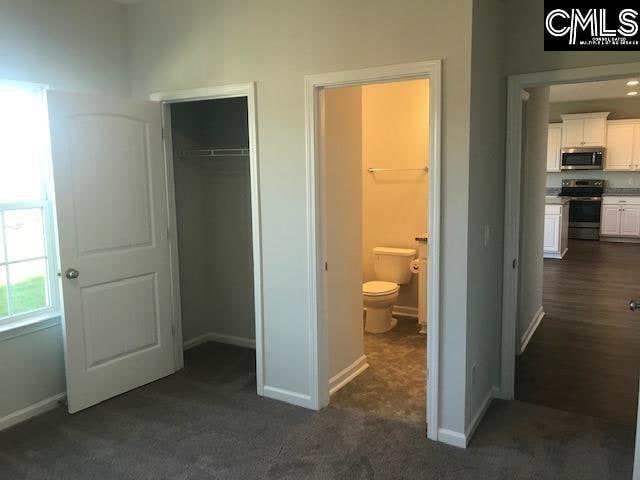 unfurnished bedroom featuring a closet, ensuite bathroom, a spacious closet, and dark colored carpet