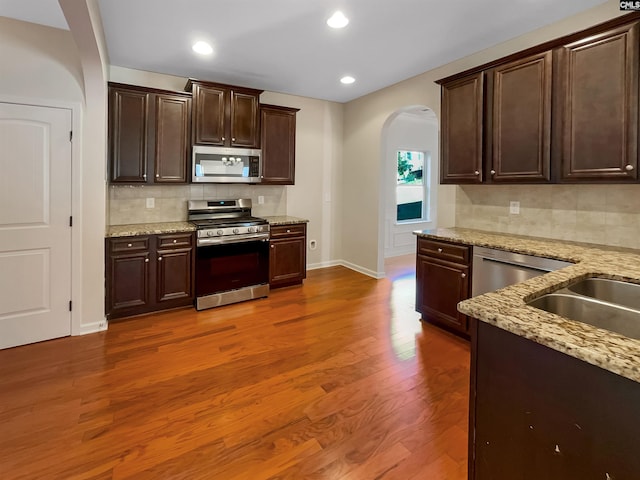 kitchen featuring tasteful backsplash, dark brown cabinets, light stone countertops, dark hardwood / wood-style floors, and stainless steel appliances