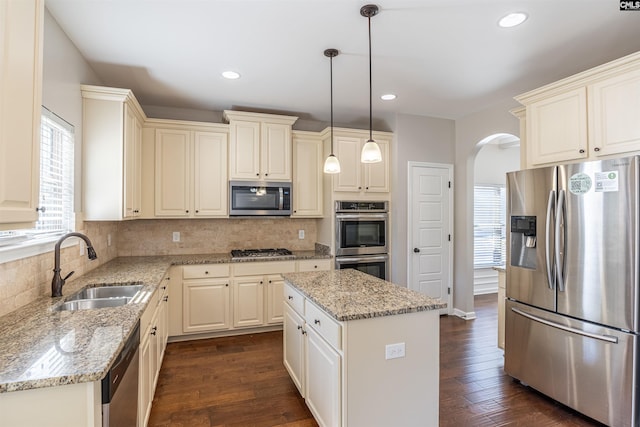 kitchen featuring dark wood-type flooring, sink, a center island, decorative light fixtures, and appliances with stainless steel finishes