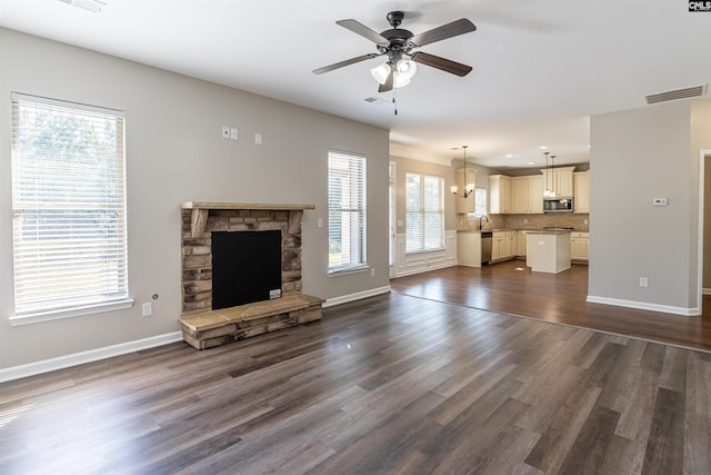 unfurnished living room featuring dark wood-type flooring, a fireplace, ceiling fan with notable chandelier, and a healthy amount of sunlight