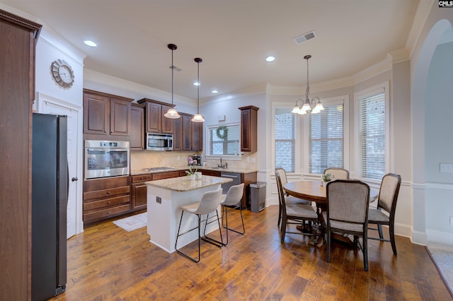 kitchen featuring hanging light fixtures, dark hardwood / wood-style flooring, light stone countertops, stainless steel appliances, and a center island