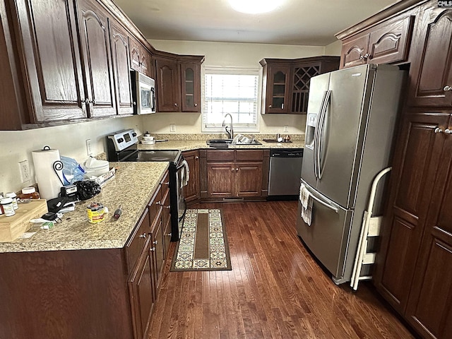 kitchen featuring appliances with stainless steel finishes, sink, light stone countertops, dark brown cabinets, and dark wood-type flooring