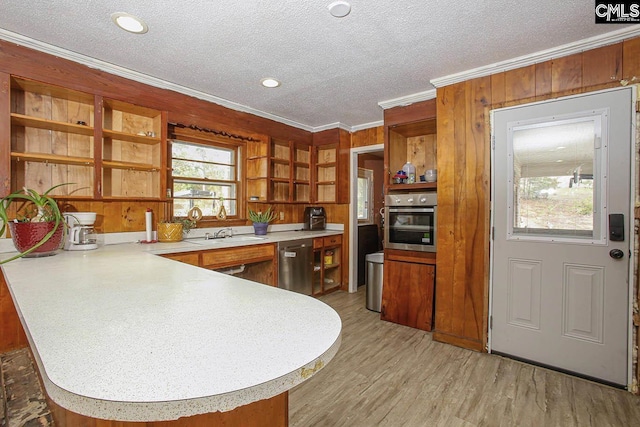 kitchen featuring kitchen peninsula, ornamental molding, stainless steel appliances, wooden walls, and light hardwood / wood-style floors