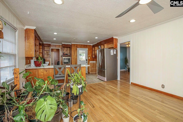 kitchen featuring light hardwood / wood-style flooring, kitchen peninsula, crown molding, wood walls, and appliances with stainless steel finishes