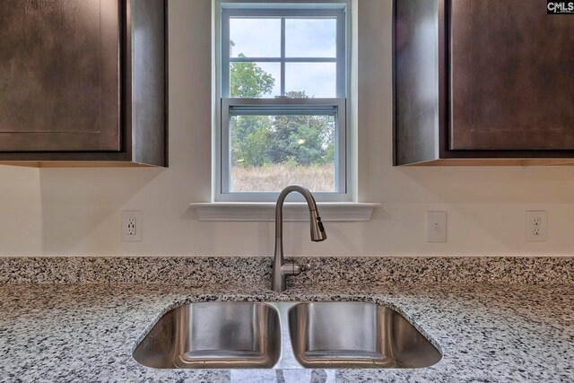 details featuring dark brown cabinetry, light stone counters, and sink