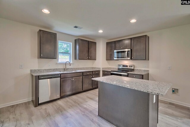 kitchen with sink, stainless steel appliances, dark brown cabinets, a kitchen island, and light wood-type flooring