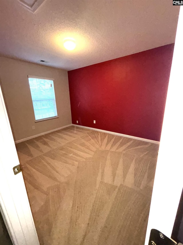 carpeted empty room with visible vents, a textured ceiling, and baseboards