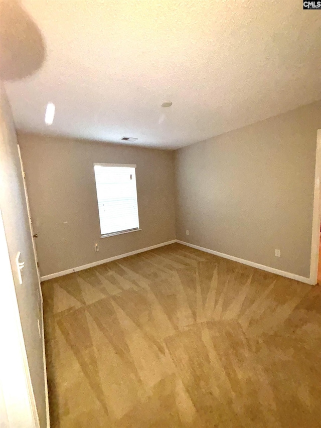 empty room with light colored carpet, a textured ceiling, and baseboards