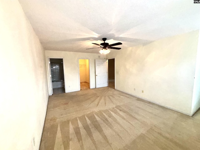 unfurnished bedroom with a walk in closet, light carpet, a closet, a textured ceiling, and a ceiling fan