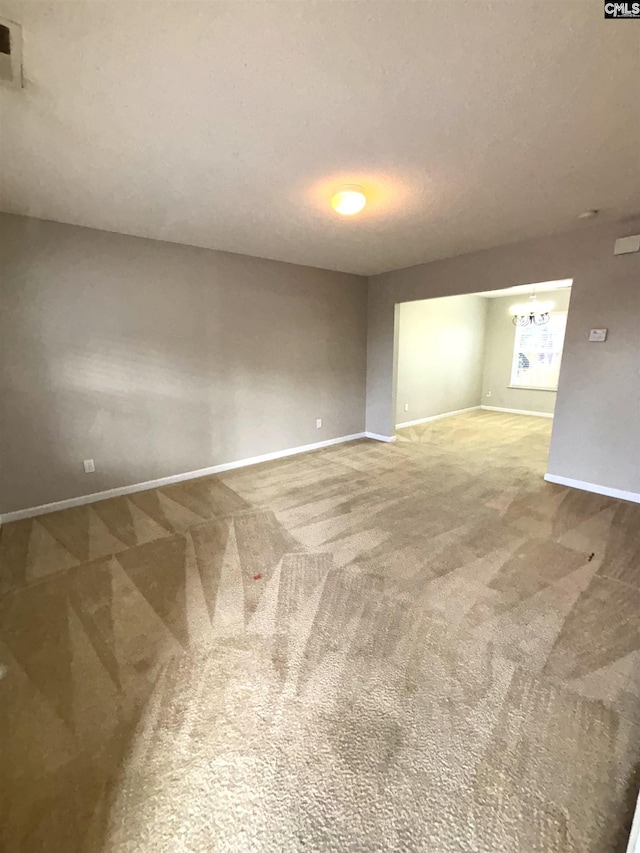 carpeted spare room with baseboards, a textured ceiling, and a chandelier