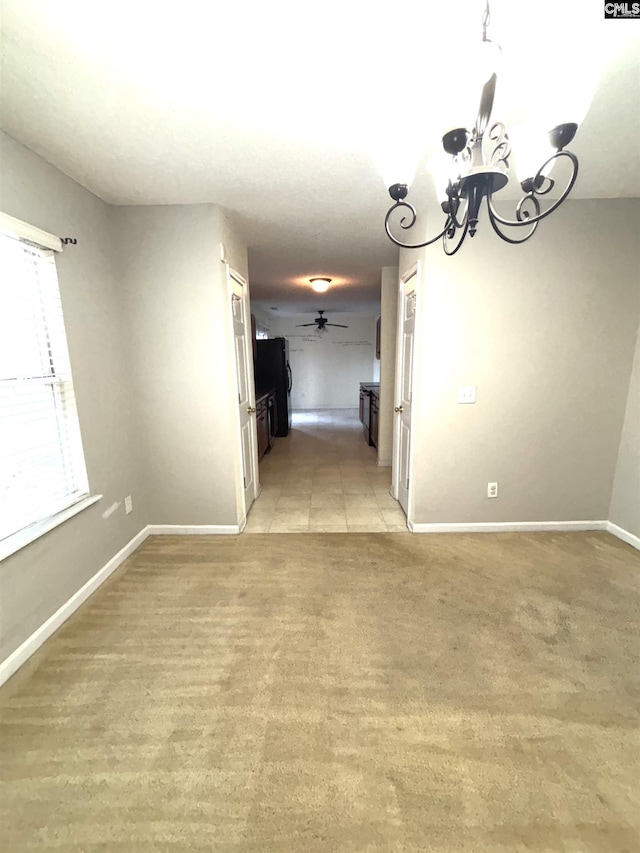 unfurnished dining area with ceiling fan with notable chandelier, light colored carpet, and baseboards