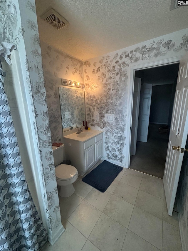 bathroom with visible vents, a textured ceiling, and wallpapered walls