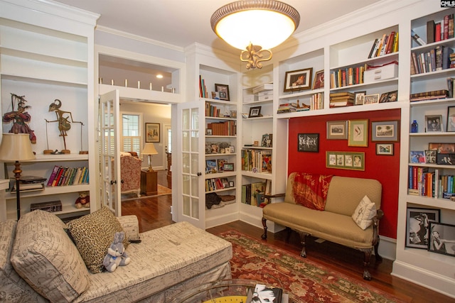 living area featuring dark wood-type flooring, ornamental molding, and built in shelves