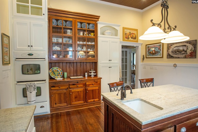 kitchen featuring sink, double oven, dark hardwood / wood-style flooring, pendant lighting, and a kitchen island with sink