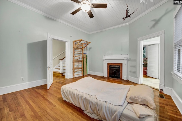 bedroom featuring a fireplace, ceiling fan, light hardwood / wood-style floors, wooden ceiling, and ornamental molding