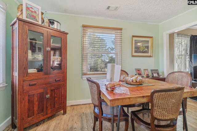 dining area featuring ornamental molding, light hardwood / wood-style flooring, and a textured ceiling