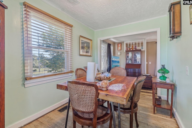 dining area featuring ornamental molding, a textured ceiling, and light hardwood / wood-style floors