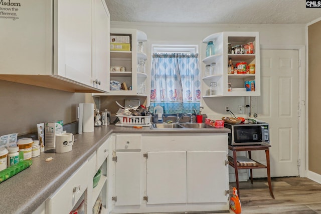 kitchen with crown molding, sink, white cabinetry, a textured ceiling, and light hardwood / wood-style floors