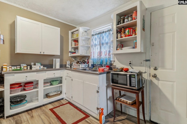 kitchen with sink, a textured ceiling, light hardwood / wood-style floors, white cabinets, and ornamental molding